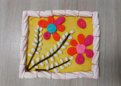 Na zdjęciu mazurek wielkanocny wykonany z pianek marshmallow oraz ozdobiony baziami i kwiatami z ciastoliny.