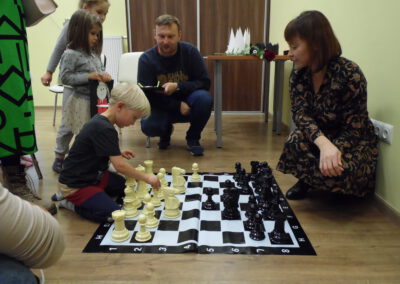Uczestnicy spotkania z cyklu Nasza Gmina Czyta Dzieciom przy dużej szachownicy ćwiczą grę w szachy